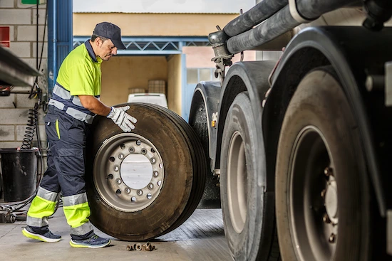 Técnico especializado en mantenimiento de flota realizando inspección y cambio de neumático en camión de carga pesada