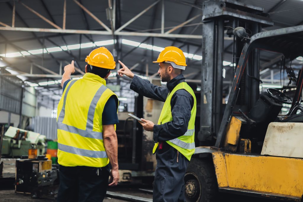 Maintenance technicians with PPE on pointing at which asset to perform maintenance on while holding a tablet with a CMMS app open in it
