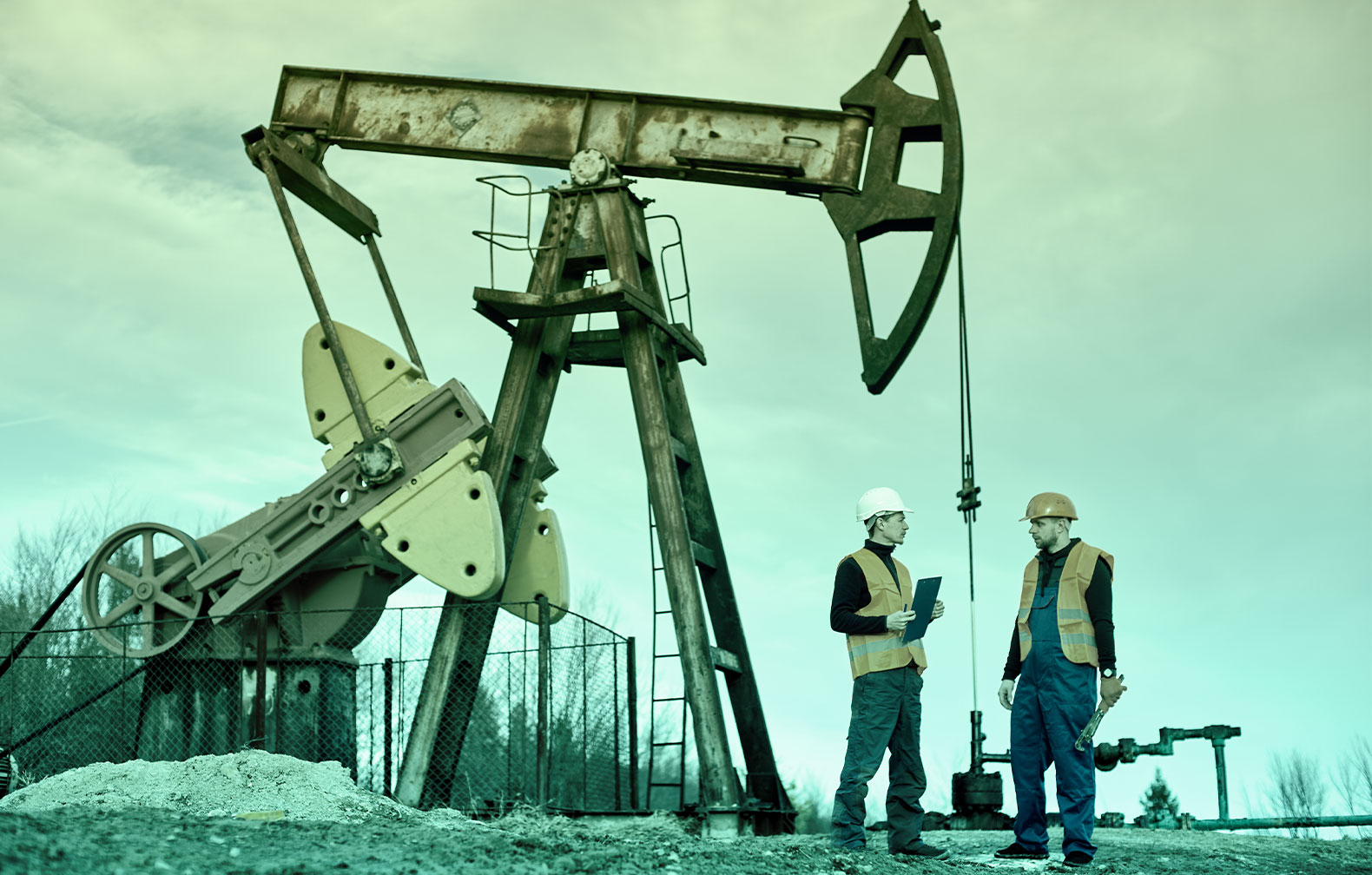 Crude Oil Pumpjack in the background and two maintenance technicians in the foreground. One is carrying a tablet with CMMShere