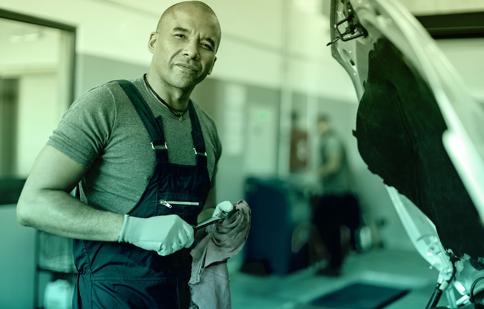 An automotive maintenance tech is holding a ratchet in his gloved hands while staring at the camera wondering why he has not subscribed to a CMMS tool such as CMMShere to make maintenance easier