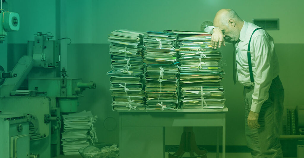 Maintenance Manager with head reclined on mountains of paperwork clamoring and regretting not getting CMMS software such as CMMShere earlier to make maintenance easier