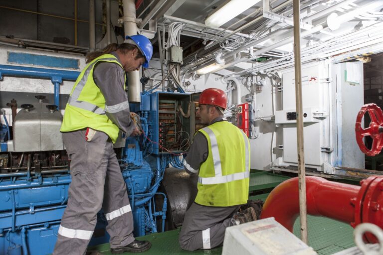 Two technicians in a pump room monitoring a switchbox and taking measurements with a multimeter to later log into the CMMS